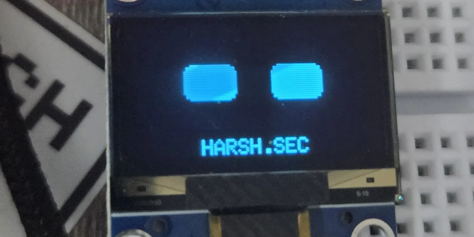 The OLED display showing its desk-pet eyes above HARSH.SEC
